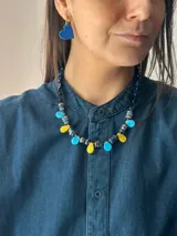 Collar corto con diseño multicolor compuesto por cuentas de cristal checo, piedras naturales y piezas de acrílico en tonos azul, celeste y amarillo, con cierre de cadena de acero quirúrgico.