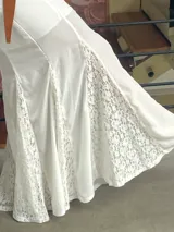 Falda larga de corte evasé en color blanco, confeccionada con paneles alternados de tela lisa y encaje floral. Presenta una caída fluida y elegante.