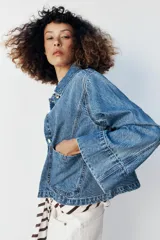 Campera de denim azul con cuello solapa, cierre frontal de botones metálicos, bolsillos delanteros de plastrón y mangas largas acampanadas.