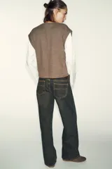 Prenda de manga larga blanca con un chaleco de tejido de punto azul marino superpuesto, creando un efecto de dos piezas. El chaleco es de cuello redondo y corte recto.