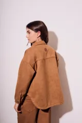 Sobrecamisa negra de estilo shacket, confeccionada en tejido de gamuza sintética. Presenta cuello camisero, cierre frontal de botones y dos bolsillos de parche con solapa en el pecho. El calce es oversize y las mangas son largas.