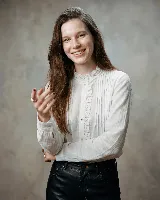 Camisa de algodón color blanco, con diseño romántico que presenta alforzas verticales y una guarda central con puntilla. Posee cuello ligeramente fruncido, mangas largas con volumen y botones frontales con detalle de cruz bordada en color chocolate.