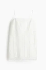 Vestido corto blanco con breteles finos ajustables, escote cuadrado y cuerpo con paneles verticales de encaje calado.