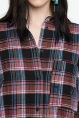 Camisa de corte recto y largo medio, confeccionada en tejido de algodón con textura. Presenta un diseño de cuadros en tonos rojo, negro y azul, cuello camisero, cierre frontal con botones, manga larga con puños abotonados y bolsillo de plastrón en el pecho.