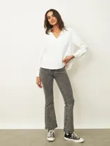 Blusa de color blanco con cuello en V y mangas largas con puños abotonados. Presenta un diseño de corte recto y holgado.