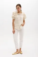 Pantalón de jean estilo mom fit en color blanco, con tiro alto, cierre frontal con botón y cremallera, y bolsillos funcionales. Presenta un diseño distintivo con un aplique fruncido en forma de espiral en la pierna derecha con costuras en contraste.