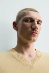 Sweater de punto en mezcla de algodón, color beige, con cuello en V y mangas largas. Presenta terminaciones en rib en cuello, puños y ruedo.