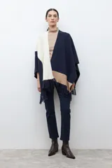 Ruana tejida con diseño color block en tonos azul marino, crudo y beige, con terminación de flecos en el ruedo.
