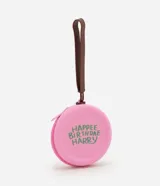 Monedero redondo de silicona color rosado con cierre de cremallera y correa de mano marrón. Presenta un estampado temático en color verde con la frase 'Happee Birthdae Harry'.