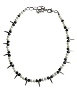 Collar de estilo punk compuesto por una alternancia de perlas de vidrio blancas y cuentas negras, intercaladas con púas metálicas plateadas. Cuenta con una cadena de ajuste de acero inoxidable.