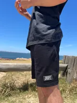 Bermuda de algodón color negro con calce relajado y cintura elastizada. Presenta un parche rectangular con el logo "DROPZ" en la parte inferior de la pierna izquierda y un largo por encima de la rodilla.