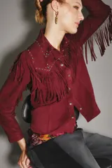 Camisa estilo western color bordó, confeccionada en gamuza caprina, con flecos largos en el canesú delantero y en las mangas. Presenta cuello con tachas metálicas plateadas.