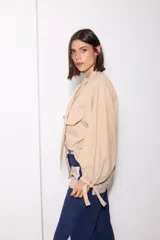 Camisa de tela afelpada color beige con nudo en el cuello, mangas abullonadas con lazos en los puños y bolsillos frontales con tapa.