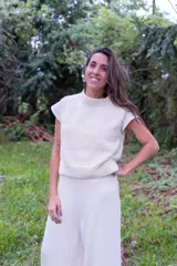 Chaleco tejido de punto en color crudo, con cuello alto y diseño sin mangas. Presenta una textura de punto grueso y corte recto.