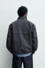 Sobrecamisa de corte regular confeccionada en mezcla de algodón y lyocell, con cuello alto y cierre frontal de cremallera. Presenta mangas largas con puños elásticos, bolsillos laterales de vivo y bajo ajustable con elástico en los laterales.