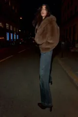 Jeans de mezclilla azul oscuro con lavado desgastado, tiro medio y corte flare ancho. Presenta un detalle de falso cierre con botones metálicos en la parte superior y costuras diagonales marcadas en la parte delantera de las piernas.