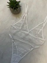 Conjunto de lencería de encaje blanco compuesto por un bralette triangular, una tanga con tiras y un portaligas integrado. El diseño presenta detalles de encaje floral y breteles regulables.
