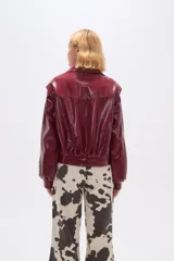 Chaqueta corta de cuero sintético negro con cuello camisero, cierre frontal con cremallera, bolsillos laterales y mangas largas abullonadas.