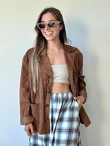 Chaqueta de estilo boho confeccionada en ecocuero agamuzado, con diseño de flecos en el frente, cierre frontal con botones y bolsillos laterales. Presenta un corte holgado y forro interior.