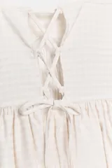 Vestido mini de escote redondo y tirantes finos en color beige con estampado de cuadros vichy. Presenta detalle de tejido tipo nido de abeja en el torso y bajo acabado tipo globo.