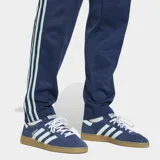 Pantalón deportivo Adidas de la colección Originals, inspirado en la selección de fútbol de Alemania. Es de color azul marino con las icónicas tres tiras laterales en color celeste. Presenta el escudo de la selección alemana en el muslo derecho y un corte clásico con cintura elástica y cordón de ajuste.