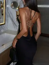 Vestido largo negro de silueta ajustada y escote halter. Presenta espalda descubierta con tiras finas y un aplique metálico con pedrería de strass.