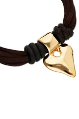 Pulsera compuesta por múltiples hilos trenzados de efecto seda marrón y tiras de cuero negro, con un dije central metálico dorado con forma de corazón estilizado. Cuenta con cierres y argollas de metal dorado.