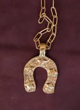 Collar de bronce dorado con cadena de eslabones rectangulares y dije grande en forma de herradura con textura arrugada.