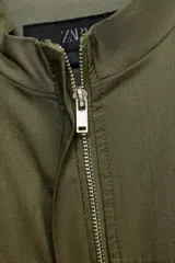 Vestido corto de estilo utilitario en color verde militar, confeccionado en gabardina. Presenta cuello redondo, cierre frontal con cremallera oculta, mangas cortas con detalle de trabilla y botón, y bolsillos de plastrón en el frente.