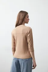 Remera de manga larga color beige, confeccionada en algodón, con escote en V y cartera corta de botones blancos.