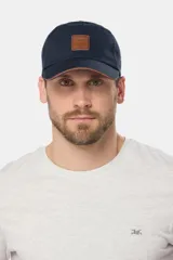 Gorro con visera curva de lona azul marino, con parche frontal de cuero sintético con el logo grabado de la marca y detalle de ribete en el borde de la visera.