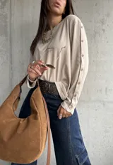 Remera de lanilla color beige, de corte holgado y manga larga. Presenta una hilera de botones decorativos a lo largo de toda la parte externa de las mangas.