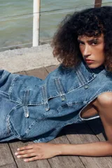 Top de denim blanco sin mangas, con cuello mao y cierre frontal cruzado con trabillas y botones metálicos.