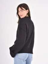 Buzo de tejido de punto color negro, con cuello redondo, mangas largas con puños anchos y ruedo acanalado.