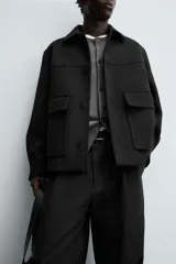 Chaquetón de corte regular fit en color negro, con cuello solapa, manga larga y cierre frontal con botones. Presenta dos bolsillos delanteros de plastrón con solapa en la cadera.