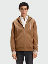 Buzo canguro con cierre frontal, color camel, con capucha y cordones trenzados. Presenta puños y ruedo con terminación de rib con franjas blancas y negras.