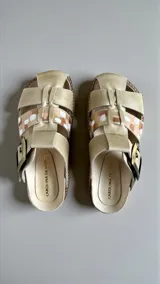 Sandalias de cuero color beige con arte pintado a mano en tonos marrones y blancos, hebilla lateral y suela de corcho y goma.