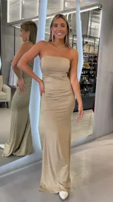 Vestido largo strapless de color dorado con acabado brillante, de corte ajustado y diseño drapeado en el torso.