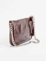 Cartera pequeña de cuero color beige, de diseño estructurado con base redondeada, cierre superior con tirador de cuero y correa de cadena metálica plateada.