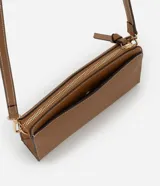 Cartera bandolera pequeña de formato rectangular, confeccionada en poliuretano color tostado con costuras decorativas en contraste. Cuenta con cierre superior de cremallera con tirador alargado, placa metálica frontal con logo y correa larga ajustable y desmontable mediante mosquetones.