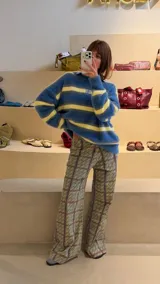 Pantalón de corte recto y tiro medio con estampado geométrico en tonos amarillos, verdes y violetas. Presenta un diseño de líneas verticales que forman cuadros y un patrón repetitivo de letras.