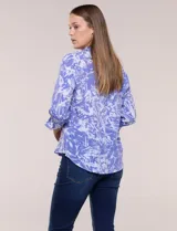 Blusa azul con estampado tipo pincelada en tonos blancos, cuello solapa con escote en V, media abotonadura frontal con botones nacarados, mangas tres cuartos con puños elásticos y diseño semi holgado.