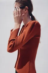 Chaqueta de punto color óxido, con cuello redondo, manga larga abullonada y cierre frontal con botones.