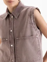 Chaleco de denim color marrón, con cuello camisero, cierre frontal con broches metálicos y bolsillos delanteros parcheados.