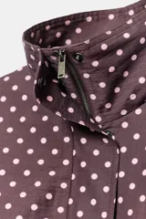 Cazadora negra con estampado de lunares blancos, cuello subido, manga larga, bolsillos delanteros, bajo ajustable con cordones y cierre frontal con cremallera y solapa con botones ocultos.