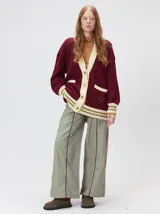 Cardigan de punto trenzado en color negro con detalles en color crema en los bolsillos, puños y ruedo. Presenta un diseño oversize, cierre frontal con botones y bordado decorativo en uno de los bolsillos delanteros.