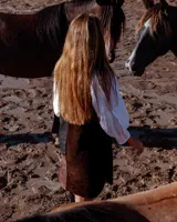 Vestido corto de corte recto y sin mangas, confeccionado en estilo patchwork con paneles de gamuza y cuero en tonos chocolate y negro. Presenta un diseño asimétrico y detalles bordados a tono en la parte frontal y trasera.