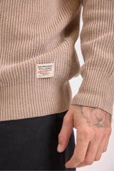 Sweater de punto grueso en color marrón, con cuello redondo y diseño de textura acanalada. Presenta un corte holgado y mangas largas.