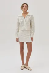 Cárdigan tejido de punto calado color crudo, con cuello polo, cierre metálico frontal y mangas largas.