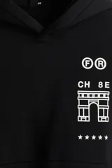 Canguro negro de corte holgado con capucha, bolsillo frontal tipo canguro y puños acanalados. Presenta un estampado gráfico minimalista en color blanco en el pecho que incluye letras, un ícono arquitectónico y estrellas.